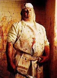 שוחט בבגדים לבנים מכוסה בדם וגם על קירות המבנה מרוחים קווי דם מעורבלים.